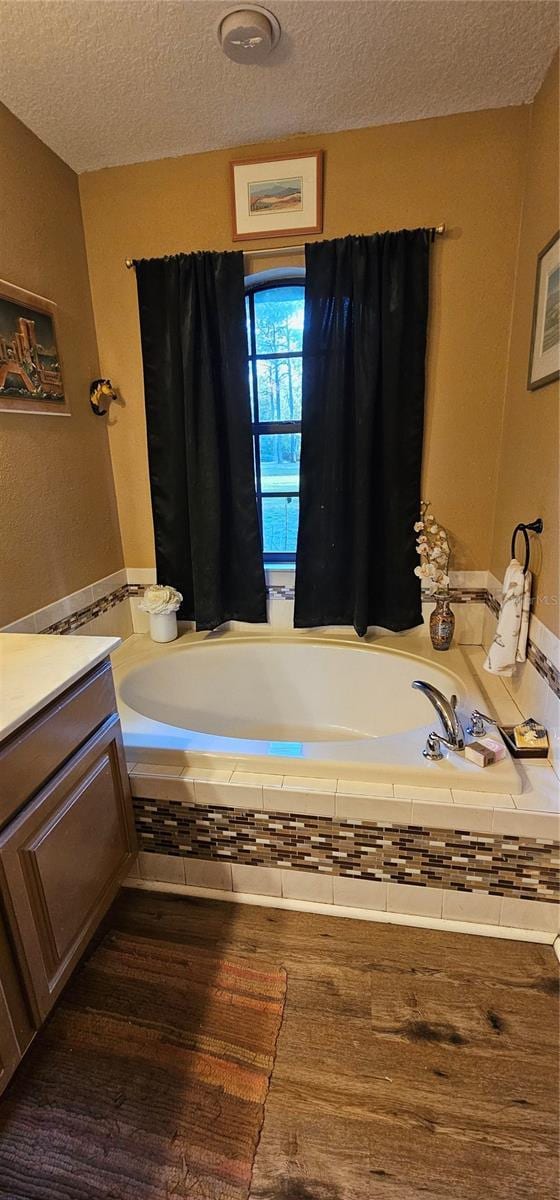 full bathroom featuring wood finished floors, a textured ceiling, a bath, and vanity