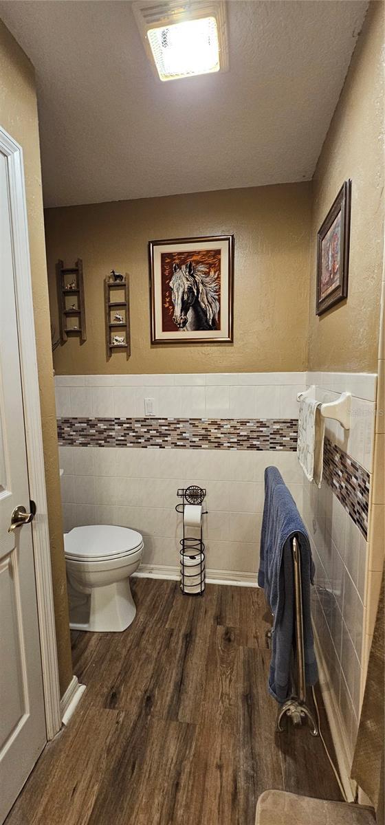 bathroom featuring a textured ceiling, toilet, tile walls, wood finished floors, and wainscoting