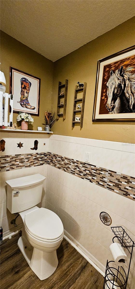 bathroom with tile walls, wood finished floors, toilet, and a textured ceiling