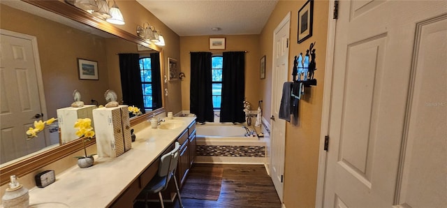 bathroom featuring wood finished floors, double vanity, a bath, a sink, and a textured ceiling