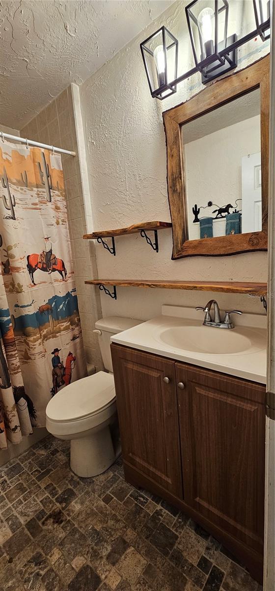 full bath with a textured ceiling, a textured wall, a shower with shower curtain, toilet, and vanity