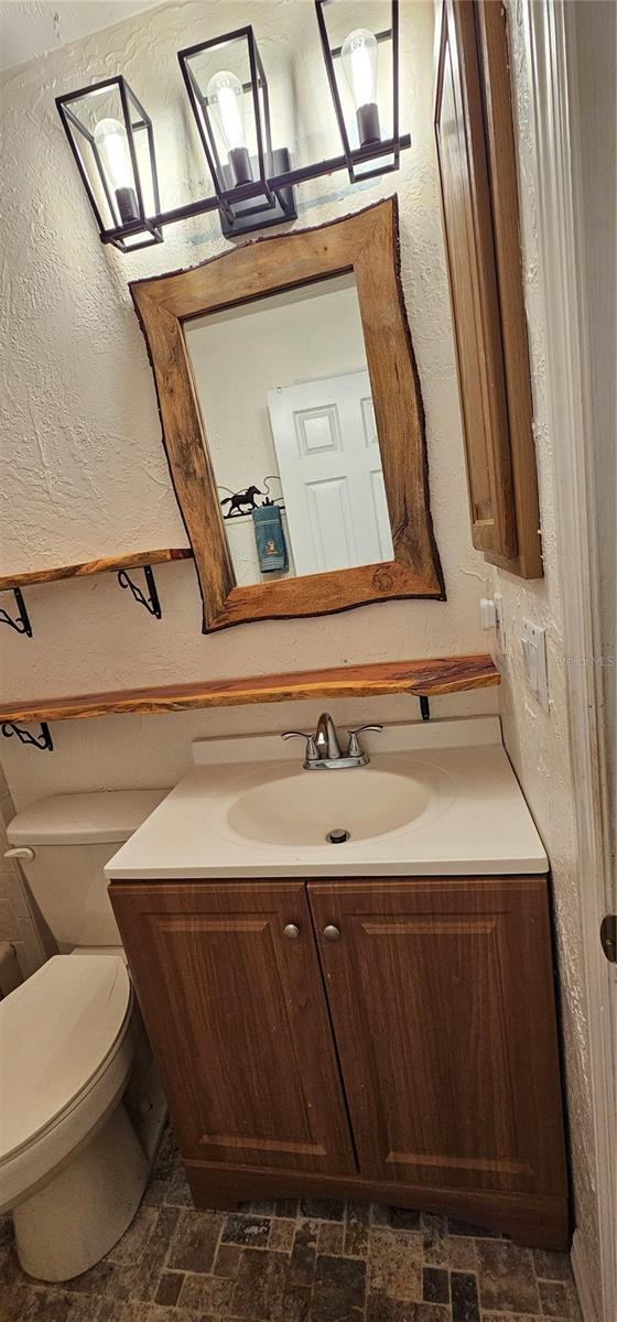 half bathroom featuring vanity, toilet, a textured wall, and brick floor