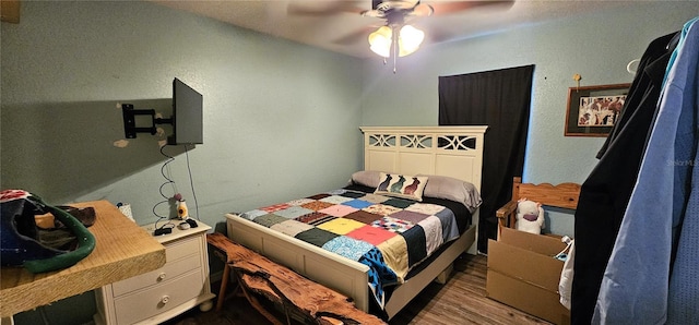 bedroom featuring a ceiling fan, a textured wall, and dark wood finished floors