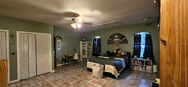 bedroom featuring attic access, ceiling fan, two closets, a textured ceiling, and brick floor
