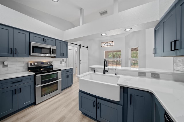 kitchen with a barn door, backsplash, stainless steel appliances, and a sink