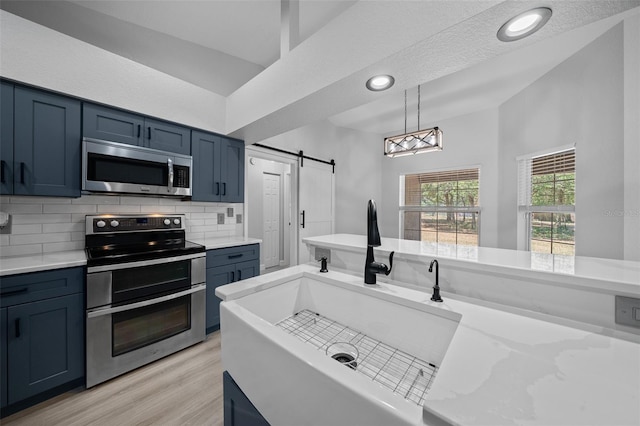 kitchen with blue cabinets, a sink, tasteful backsplash, a barn door, and appliances with stainless steel finishes