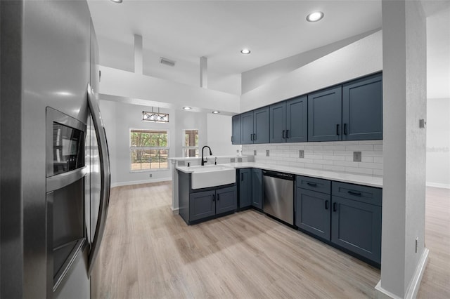 kitchen featuring light wood finished floors, a peninsula, a sink, and appliances with stainless steel finishes