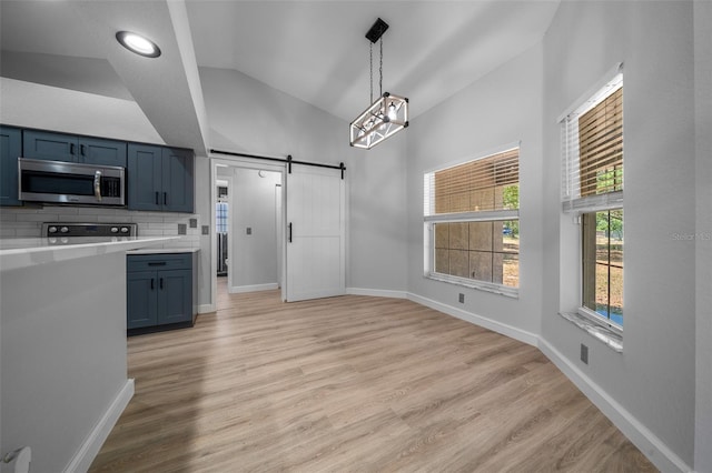 kitchen with blue cabinets, stainless steel microwave, a barn door, lofted ceiling, and light countertops