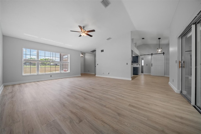 unfurnished living room with a barn door, vaulted ceiling, light wood-type flooring, ceiling fan, and visible vents