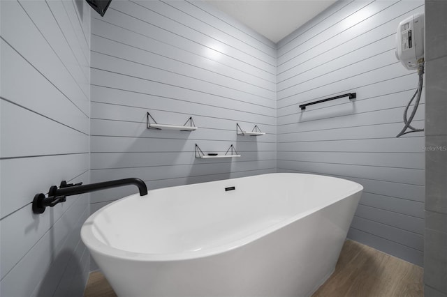 bathroom with wood walls, a freestanding tub, and wood finished floors