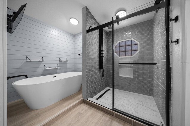 bathroom with a shower stall, a soaking tub, and wood finished floors