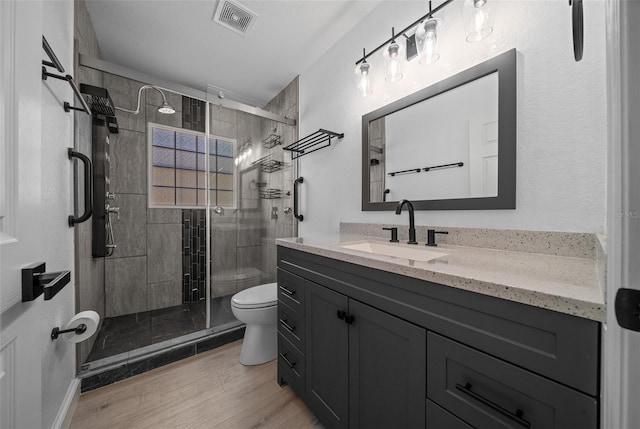 bathroom with wood finished floors, a stall shower, vanity, toilet, and visible vents