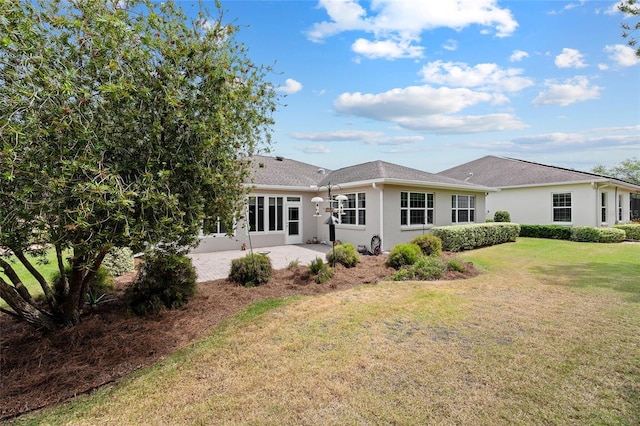 rear view of house with stucco siding, a yard, and a patio