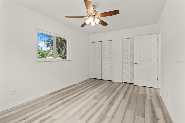 unfurnished bedroom featuring light wood-style floors, two closets, a ceiling fan, and baseboards