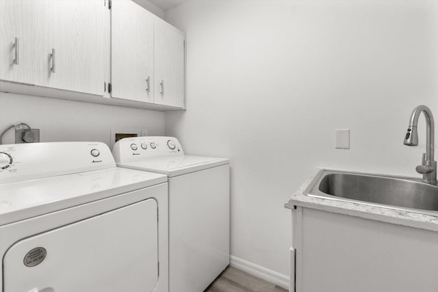 clothes washing area featuring a sink, cabinet space, light wood-style flooring, washing machine and dryer, and baseboards