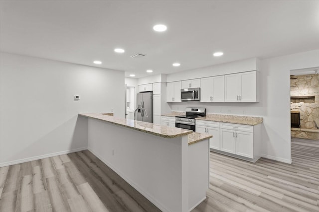 kitchen featuring a peninsula, white cabinetry, light wood-style flooring, baseboards, and appliances with stainless steel finishes