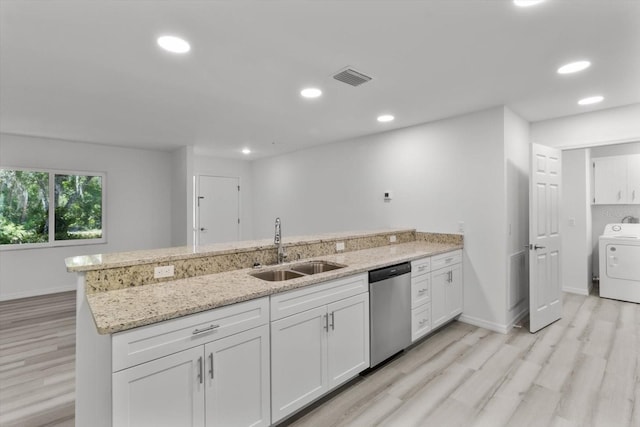 kitchen with a sink, dishwasher, washer / dryer, light wood finished floors, and a peninsula