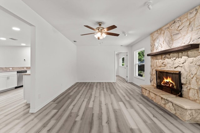 unfurnished living room with light wood-style flooring, ceiling fan, a fireplace, baseboards, and visible vents