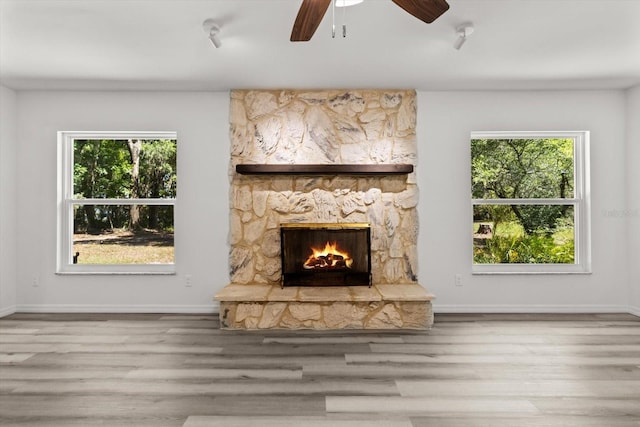 unfurnished living room featuring a fireplace, wood finished floors, a wealth of natural light, and ceiling fan