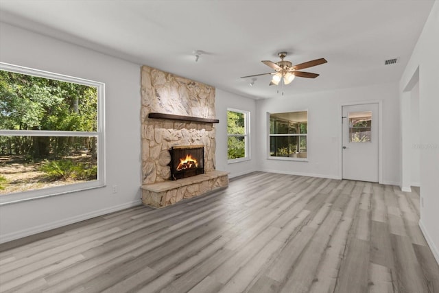 unfurnished living room featuring a stone fireplace, visible vents, a ceiling fan, wood finished floors, and baseboards