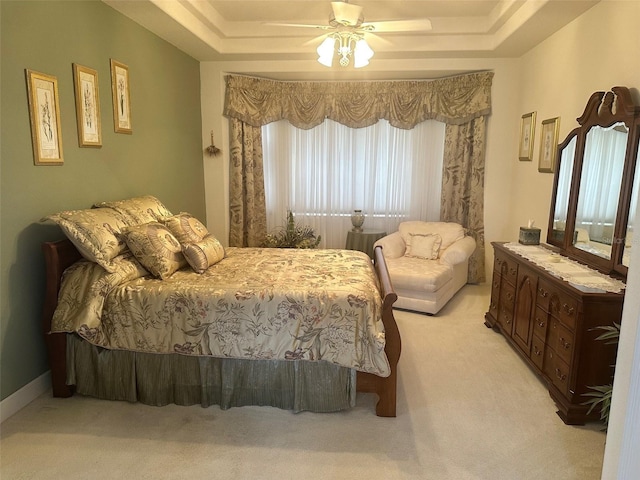 bedroom with a tray ceiling, a ceiling fan, and light carpet