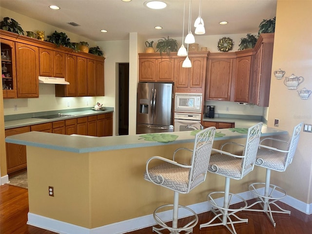 kitchen featuring dark wood-type flooring, a kitchen bar, under cabinet range hood, and white appliances