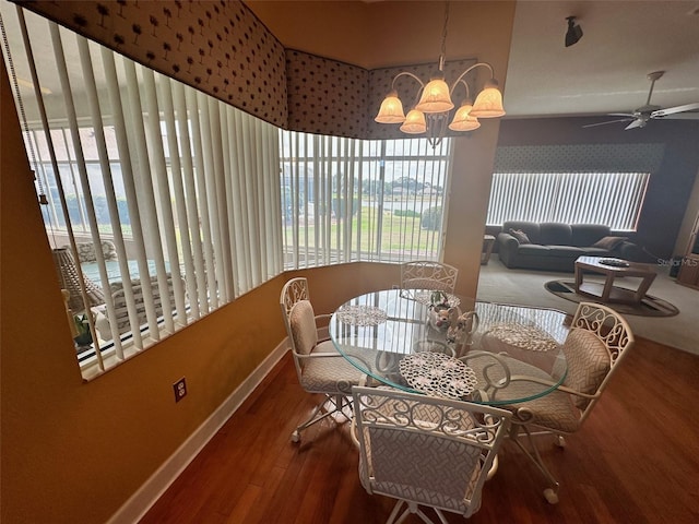 dining space with ceiling fan with notable chandelier, baseboards, wood finished floors, and a wealth of natural light