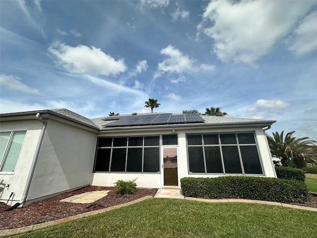 back of house with roof mounted solar panels, a lawn, and stucco siding