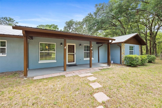 rear view of property with a lawn, stucco siding, and metal roof