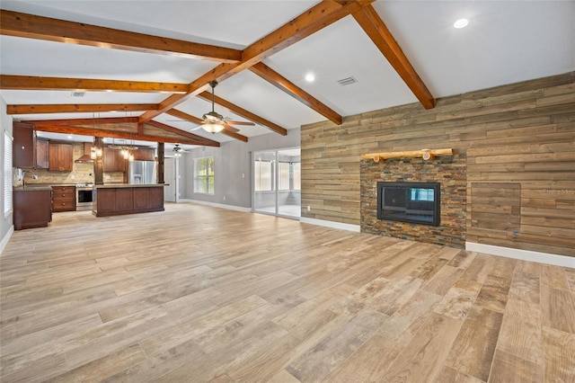 unfurnished living room featuring a ceiling fan, a stone fireplace, light wood-type flooring, and vaulted ceiling with beams