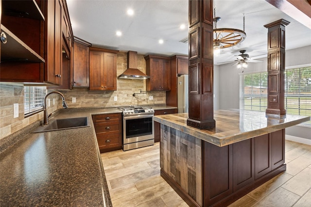 kitchen featuring wall chimney range hood, decorative columns, backsplash, appliances with stainless steel finishes, and a sink