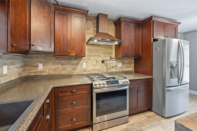 kitchen with backsplash, appliances with stainless steel finishes, dark stone counters, and wall chimney exhaust hood