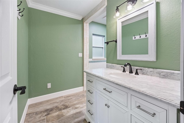 bathroom with baseboards, ornamental molding, vanity, wood finished floors, and a textured wall