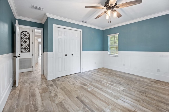 unfurnished bedroom featuring a closet, visible vents, wood finished floors, and a wainscoted wall