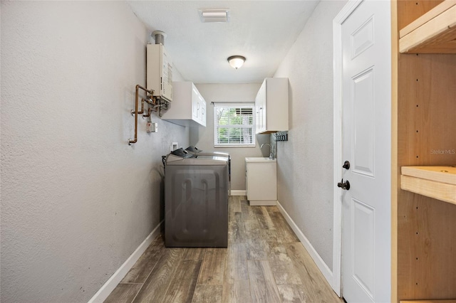laundry room featuring washing machine and dryer, baseboards, light wood finished floors, water heater, and cabinet space