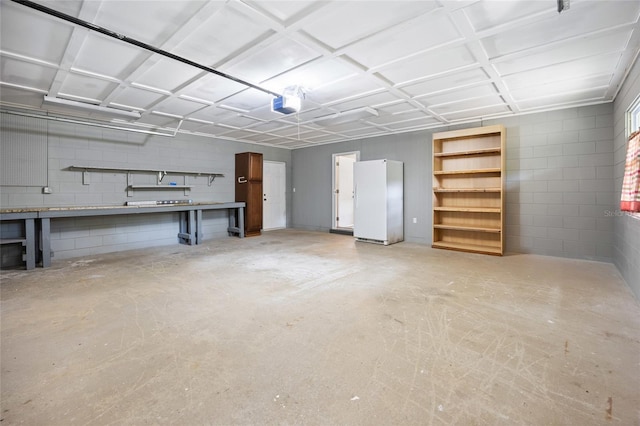 garage featuring freestanding refrigerator, a garage door opener, and concrete block wall