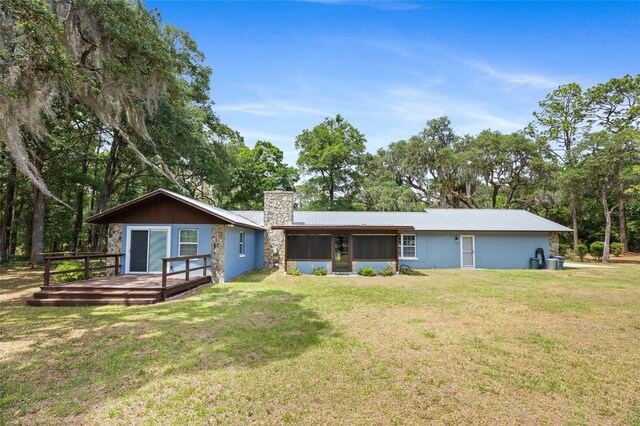 rear view of house with a chimney, a sunroom, a deck, a lawn, and metal roof