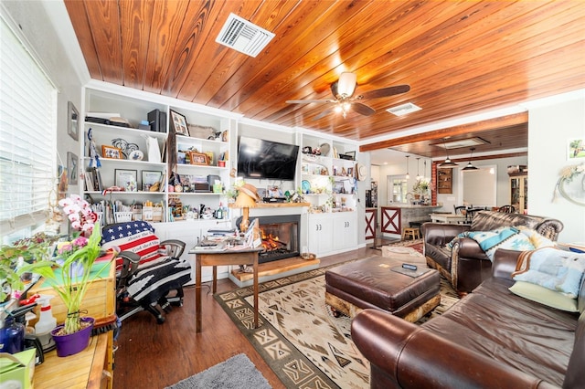 living area with a warm lit fireplace, wood finished floors, visible vents, a ceiling fan, and wood ceiling