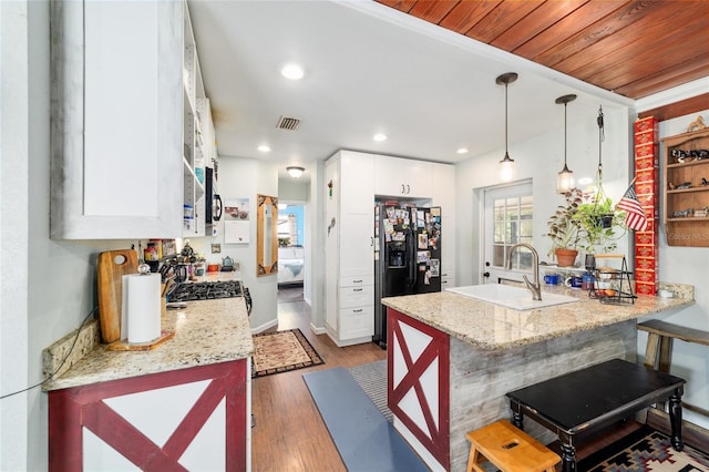 kitchen featuring a peninsula, visible vents, white cabinets, and black fridge
