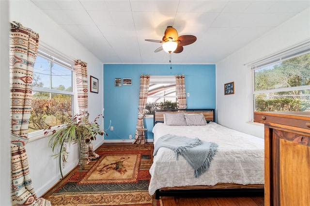 bedroom featuring wood finished floors, a ceiling fan, baseboards, and multiple windows