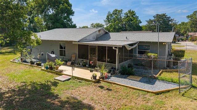 rear view of house featuring roof with shingles, fence, a deck, a yard, and a sunroom