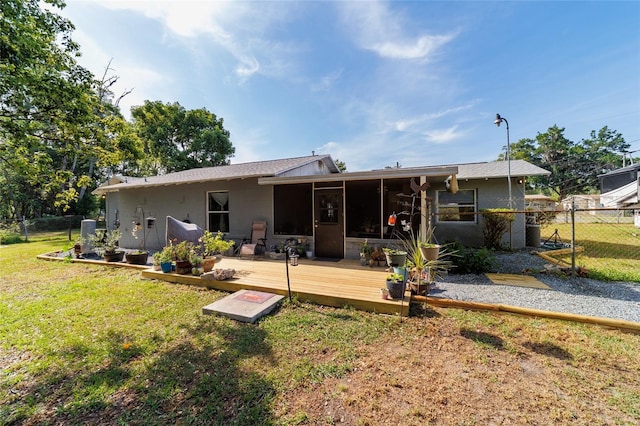 rear view of house featuring a wooden deck, a yard, a sunroom, and fence