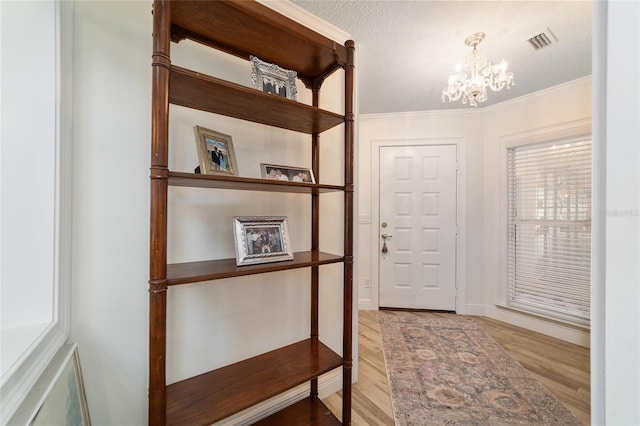 doorway with ornamental molding, wood finished floors, a chandelier, and visible vents