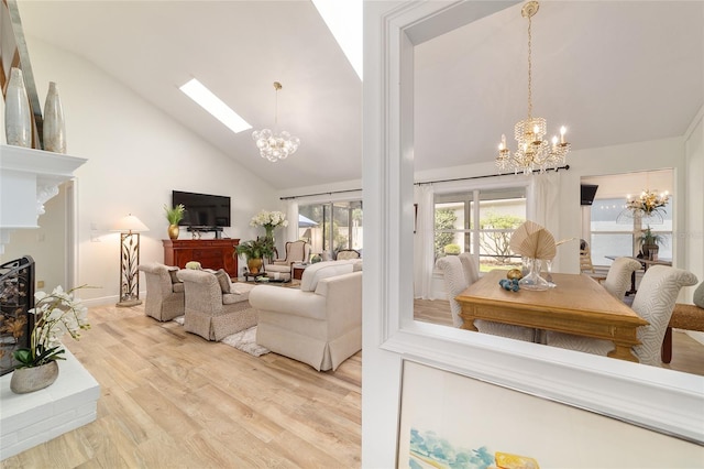 living area featuring light wood-style floors, a notable chandelier, a fireplace with raised hearth, a skylight, and high vaulted ceiling