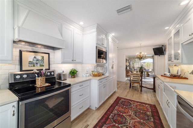 kitchen featuring an inviting chandelier, stainless steel appliances, custom range hood, white cabinetry, and visible vents