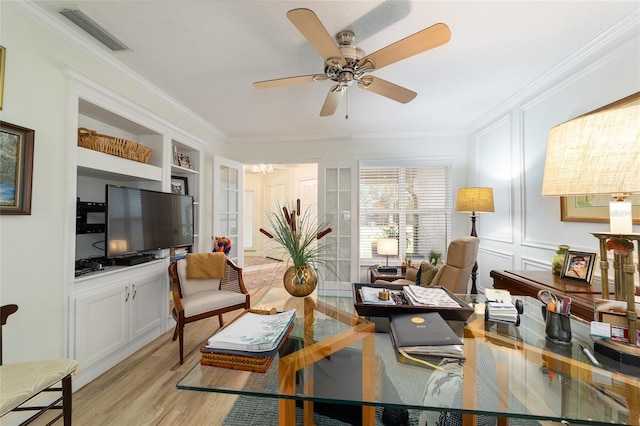 living room featuring light wood finished floors, visible vents, crown molding, built in shelves, and ceiling fan