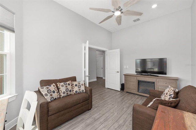 living room featuring light wood finished floors, baseboards, visible vents, ceiling fan, and high vaulted ceiling