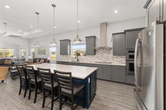 kitchen with wall chimney range hood, a sink, open floor plan, gray cabinets, and stainless steel appliances