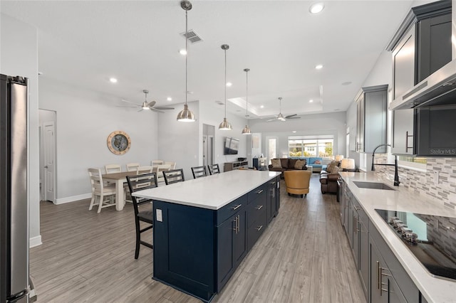 kitchen featuring a kitchen breakfast bar, a sink, open floor plan, ceiling fan, and black electric stovetop
