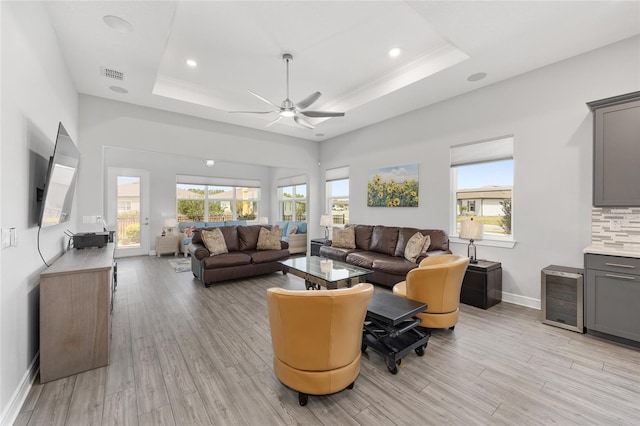 living area with wine cooler, visible vents, light wood-style floors, ceiling fan, and a raised ceiling